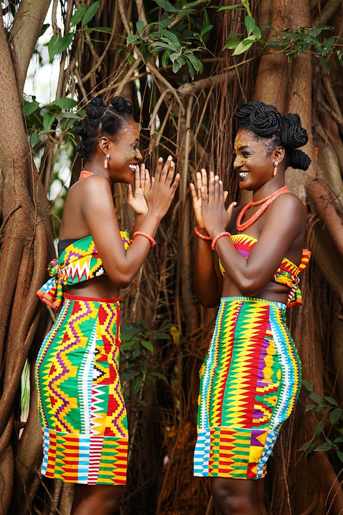 Two smiling African women in traditional vibrant clothing playing outdoors.